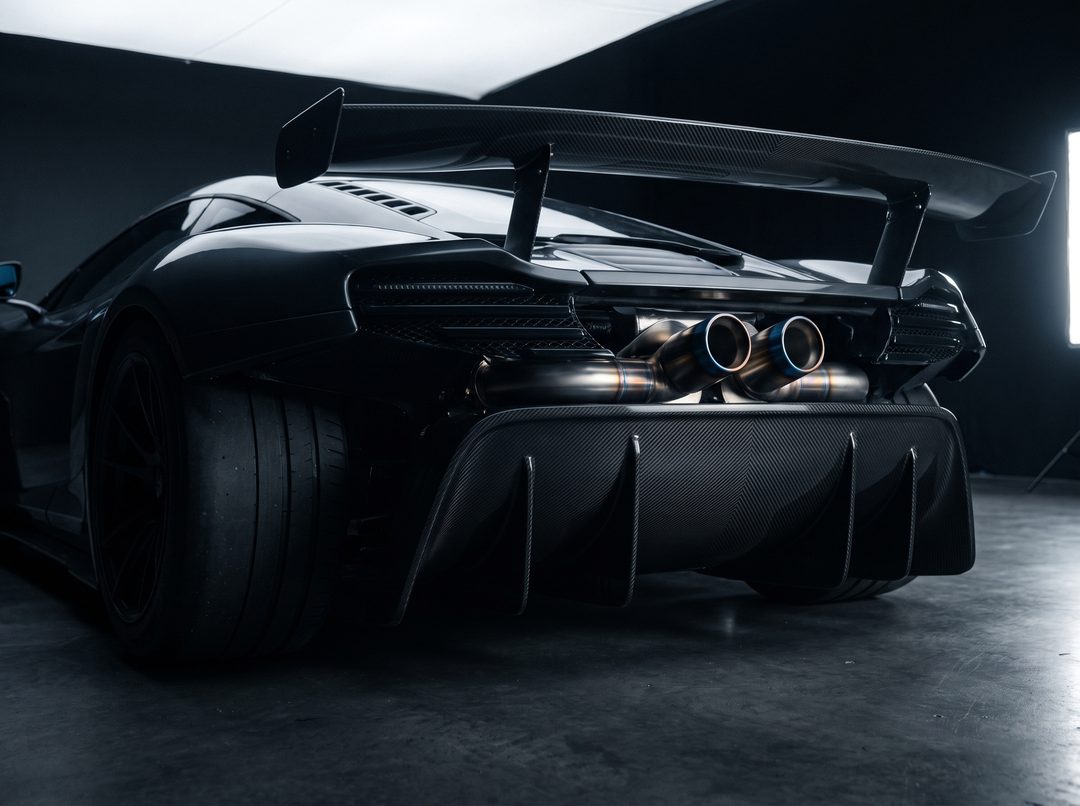 The carbon rear diffuser and titanium exhaust tips of a supercar, beneath its rear wing