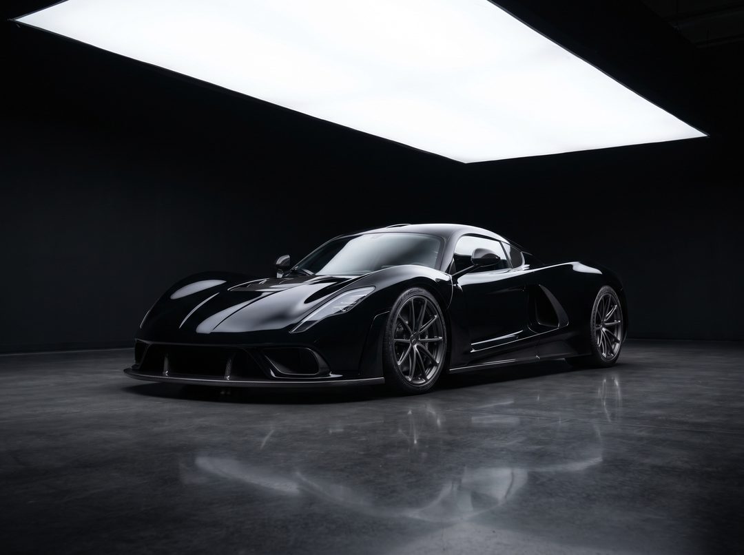 A black mid-engine supercar alone under a studio softbox, mirrored in polished concrete